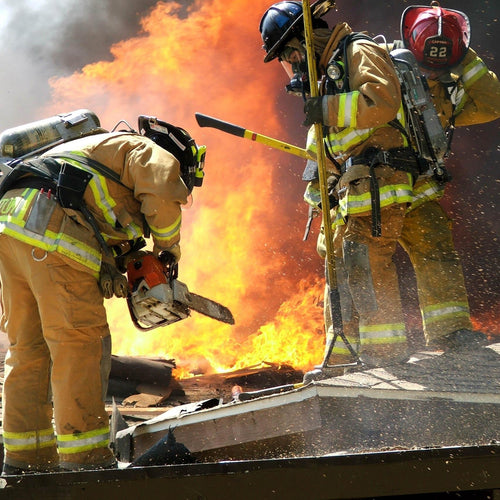 Firefighters using a chainsaw to cut through a burning structure.