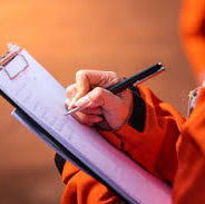Person in orange jumpsuit holding a clipboard and pen against a brown background